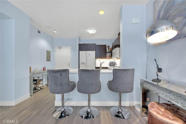 kitchen featuring a peninsula, white appliances, light wood-style floors, and a kitchen breakfast bar