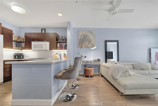 kitchen with open shelves, white microwave, a breakfast bar area, and light countertops