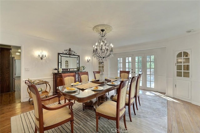 dining area featuring a notable chandelier, ornamental molding, light hardwood / wood-style flooring, and french doors