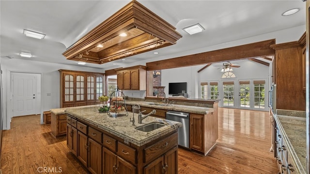 kitchen with kitchen peninsula, light wood-type flooring, stainless steel dishwasher, a kitchen island with sink, and sink