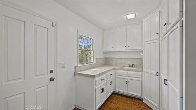 interior space with tile counters, white cabinets, dark hardwood / wood-style floors, and sink