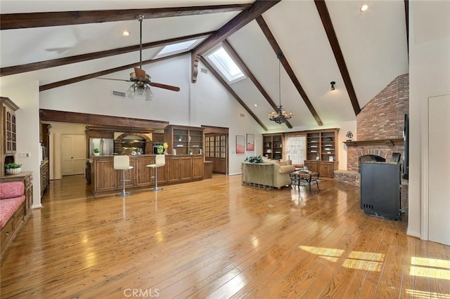 living room with a skylight, beam ceiling, high vaulted ceiling, light hardwood / wood-style flooring, and a fireplace