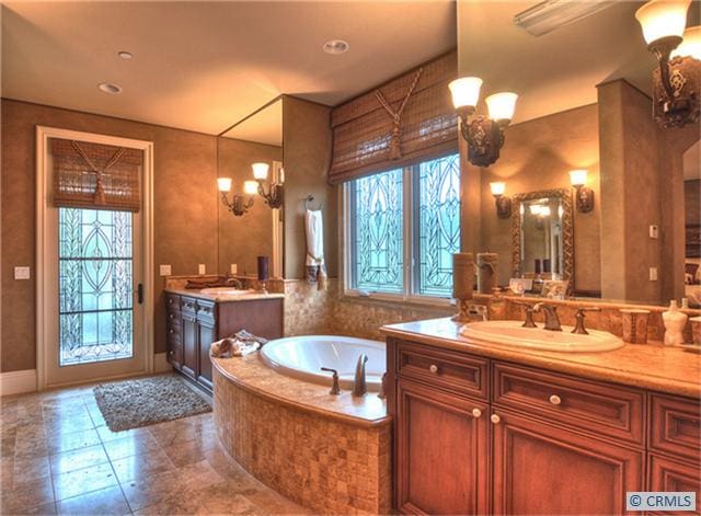 bathroom featuring vanity, tiled tub, a wealth of natural light, and an inviting chandelier