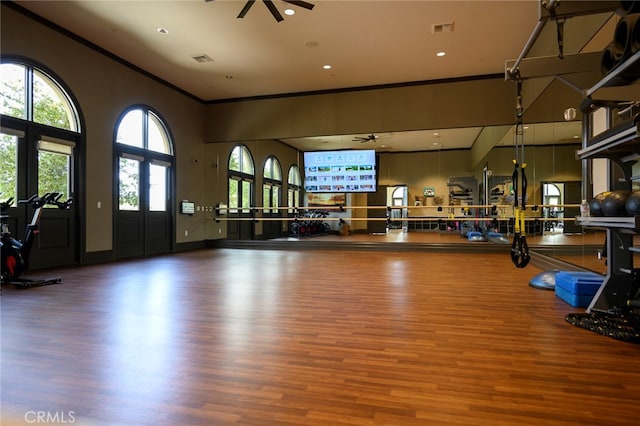 exercise room featuring ornamental molding, a towering ceiling, hardwood / wood-style flooring, and ceiling fan