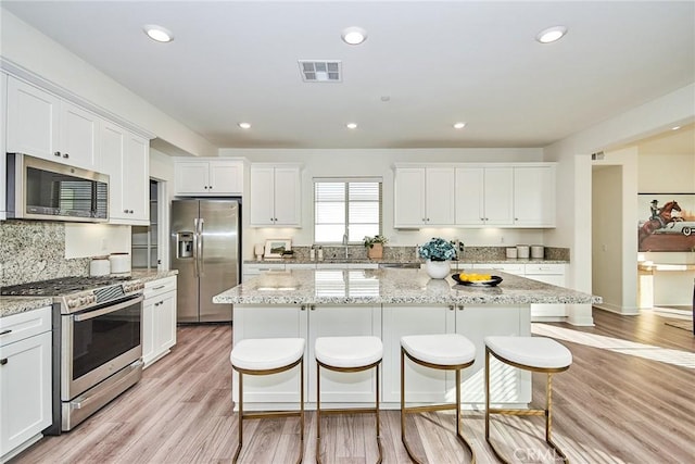 kitchen with light stone countertops, stainless steel appliances, white cabinets, light hardwood / wood-style floors, and a kitchen island