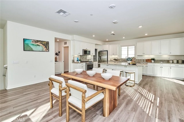 kitchen with white cabinets, light wood-type flooring, a kitchen island, light stone counters, and stainless steel appliances