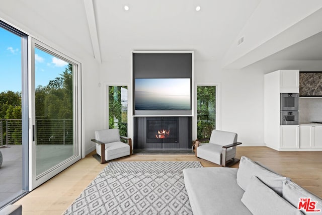 living room featuring a healthy amount of sunlight, light hardwood / wood-style flooring, and lofted ceiling with beams