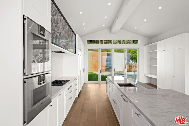 kitchen with white cabinetry, vaulted ceiling with beams, light stone countertops, double oven, and sink