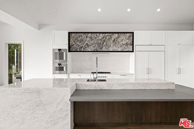 kitchen with sink, white cabinetry, paneled fridge, light stone countertops, and double oven