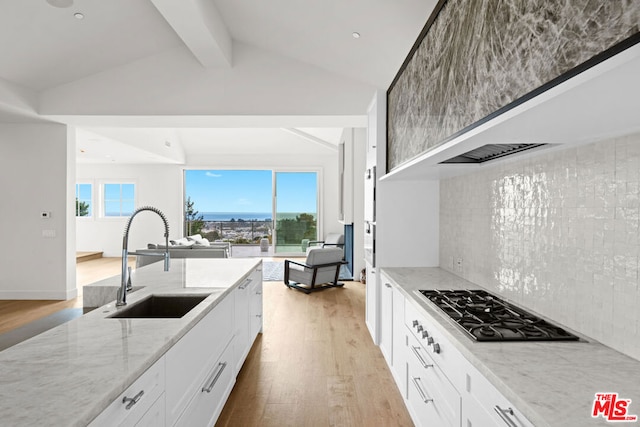 kitchen featuring white cabinetry, light wood-type flooring, vaulted ceiling with beams, light stone counters, and sink