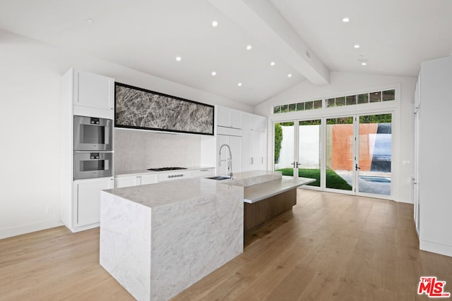 kitchen with light stone counters, sink, white cabinetry, and an island with sink