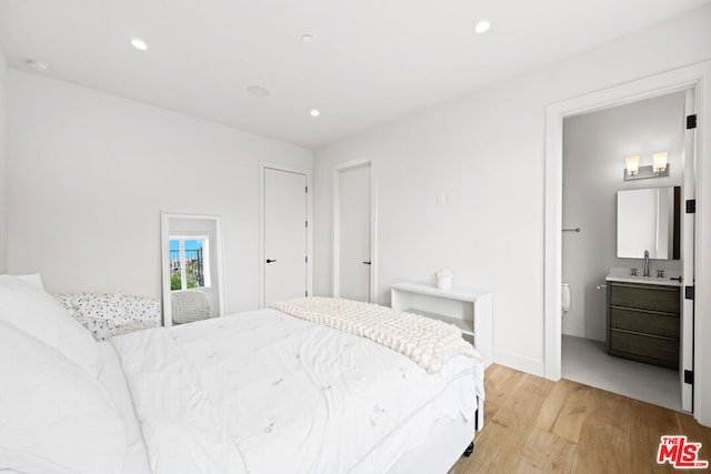 bedroom with ensuite bathroom, sink, and light hardwood / wood-style floors