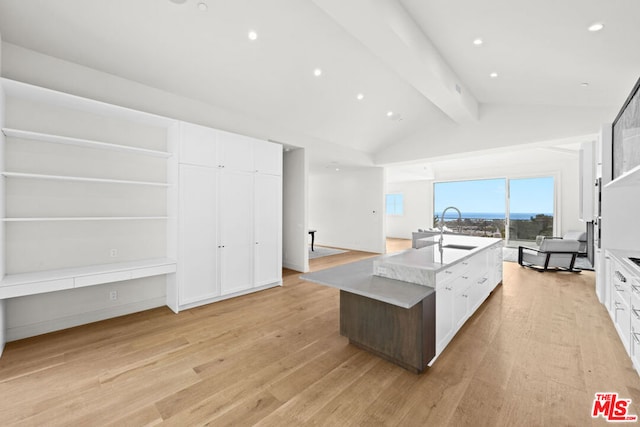 kitchen featuring white cabinets, light hardwood / wood-style flooring, sink, lofted ceiling with beams, and a center island with sink