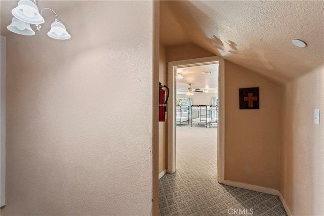 hallway featuring a textured ceiling, light carpet, and vaulted ceiling