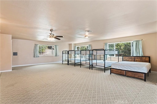 bedroom with ceiling fan, light colored carpet, and a textured ceiling