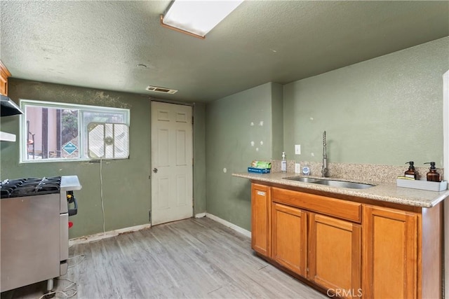 kitchen with gas range, light wood-type flooring, a textured ceiling, and sink