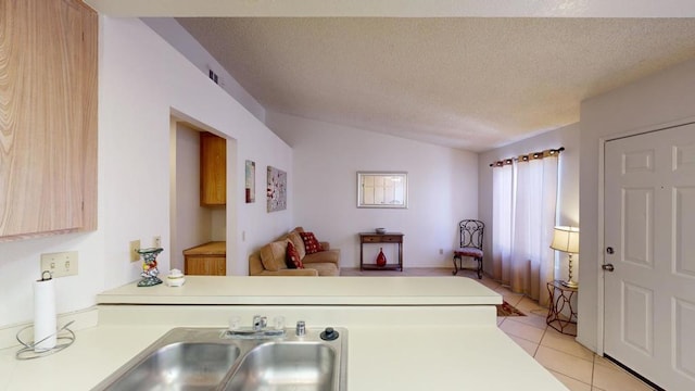 kitchen with sink, vaulted ceiling, light tile patterned floors, a textured ceiling, and kitchen peninsula