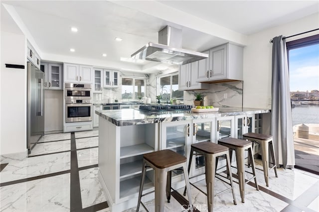 kitchen with kitchen peninsula, appliances with stainless steel finishes, tasteful backsplash, and island range hood