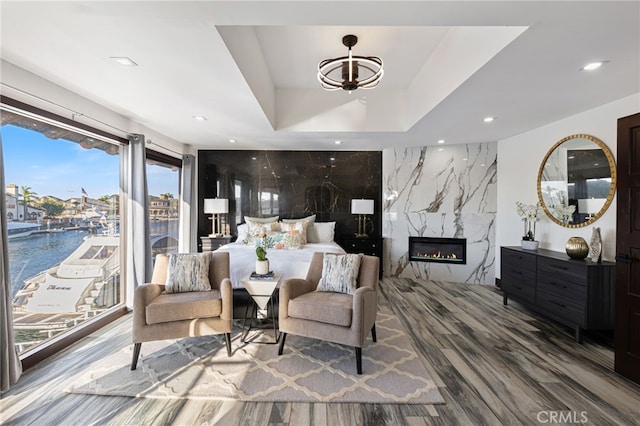 bedroom featuring a raised ceiling, a water view, hardwood / wood-style flooring, a fireplace, and a chandelier