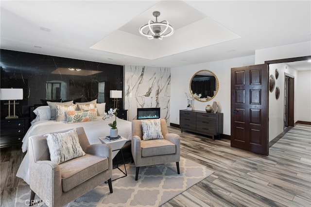 bedroom featuring hardwood / wood-style floors, a raised ceiling, and a fireplace