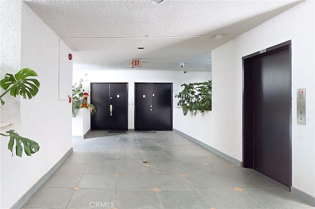 corridor with tile patterned floors, elevator, and a textured ceiling