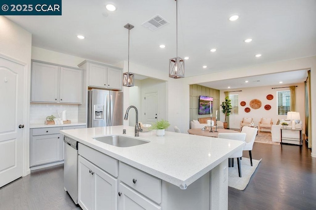 kitchen featuring pendant lighting, an island with sink, sink, stainless steel appliances, and dark wood-type flooring