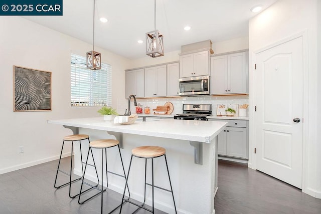 kitchen featuring hanging light fixtures, appliances with stainless steel finishes, a center island with sink, and decorative backsplash