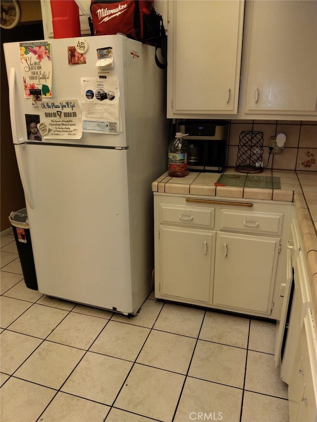 kitchen with decorative backsplash, light tile patterned floors, white cabinetry, tile counters, and white refrigerator