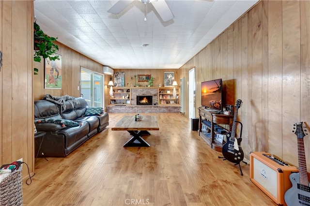 living room with ceiling fan, a fireplace, light wood-type flooring, and wood walls