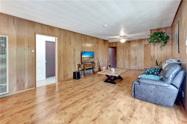 living room with ceiling fan, wood walls, and light wood-type flooring