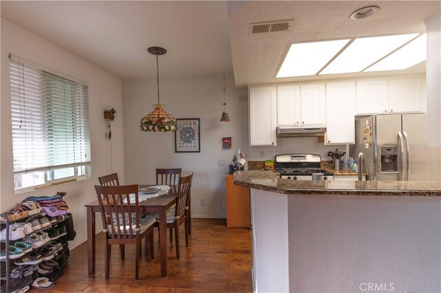 kitchen with dark stone counters, hanging light fixtures, appliances with stainless steel finishes, dark hardwood / wood-style flooring, and white cabinetry