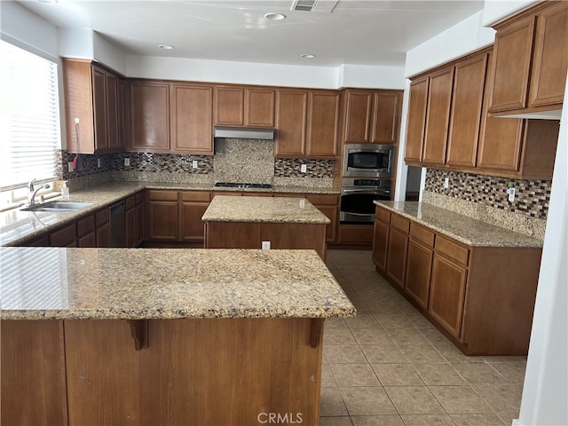 kitchen with light stone counters, backsplash, stainless steel appliances, sink, and a center island