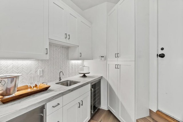 kitchen with light stone counters, white cabinetry, beverage cooler, and light hardwood / wood-style flooring