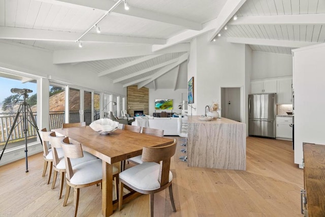 dining space featuring beam ceiling, light wood-type flooring, rail lighting, and high vaulted ceiling