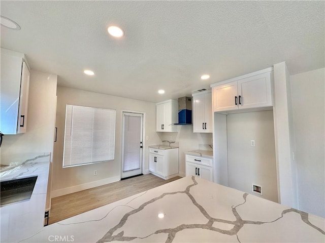 kitchen with white cabinetry, wall chimney exhaust hood, light stone counters, a textured ceiling, and light wood-type flooring