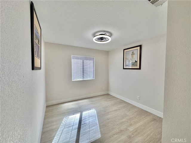 empty room featuring light wood-type flooring and a textured ceiling