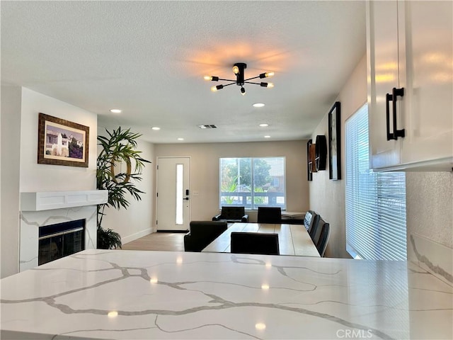 kitchen featuring light stone countertops, a high end fireplace, a textured ceiling, white cabinets, and light hardwood / wood-style floors