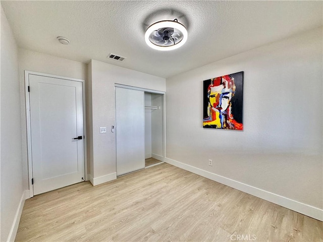 unfurnished bedroom with light wood-type flooring, a textured ceiling, and a closet