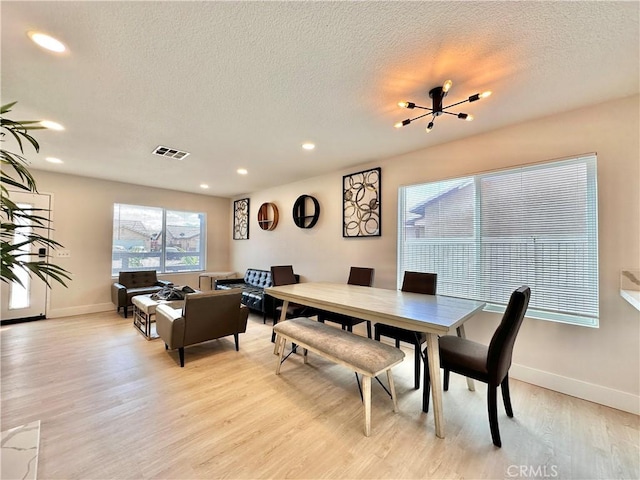 dining space with a chandelier, light hardwood / wood-style floors, and a textured ceiling