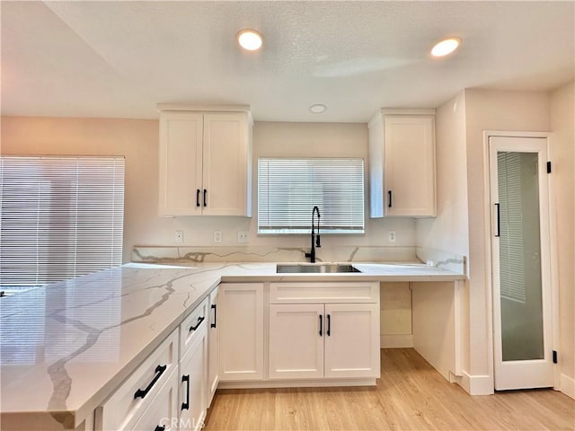 kitchen with white cabinetry, sink, light stone counters, and light hardwood / wood-style flooring