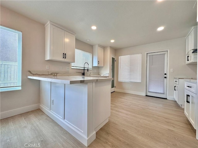 kitchen with sink, a kitchen breakfast bar, kitchen peninsula, light hardwood / wood-style floors, and white cabinets