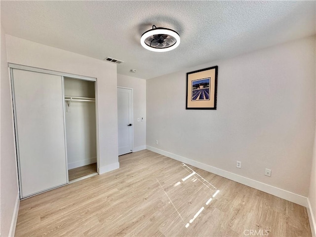 unfurnished bedroom featuring a textured ceiling, light hardwood / wood-style floors, and a closet