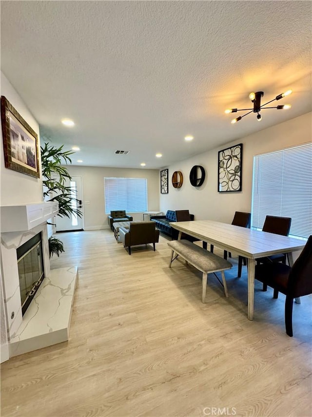 dining room with a textured ceiling, a high end fireplace, and light hardwood / wood-style flooring