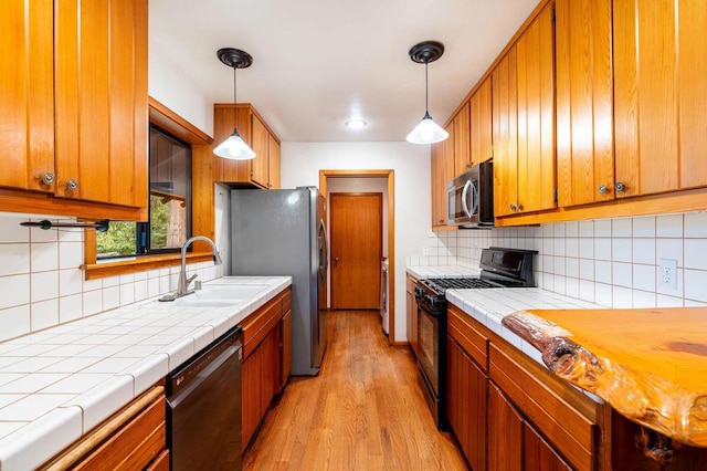 kitchen featuring black appliances, pendant lighting, light wood-type flooring, and tasteful backsplash