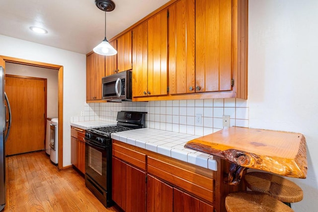 kitchen with decorative backsplash, appliances with stainless steel finishes, washing machine and clothes dryer, light hardwood / wood-style floors, and tile counters