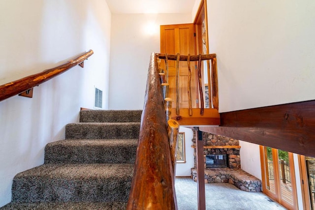 stairway with carpet flooring, a stone fireplace, and a wealth of natural light