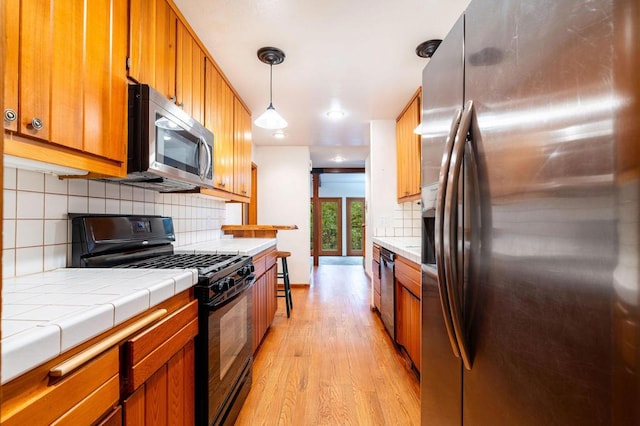 kitchen with stainless steel appliances, light hardwood / wood-style flooring, backsplash, tile countertops, and pendant lighting