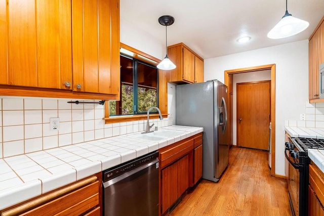 kitchen with sink, stainless steel appliances, decorative light fixtures, decorative backsplash, and light wood-type flooring