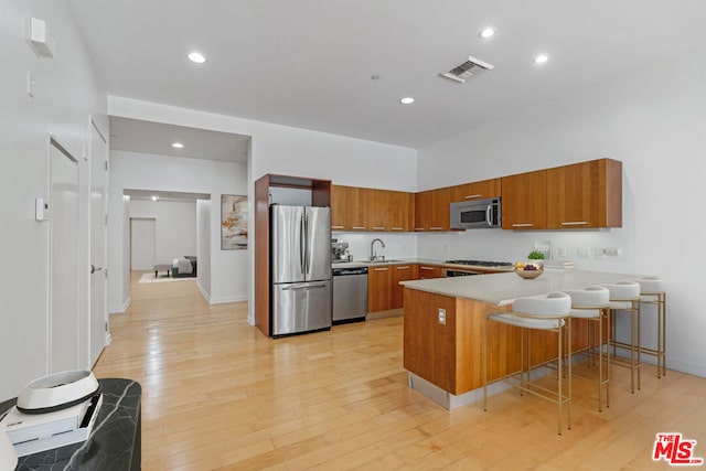 kitchen featuring kitchen peninsula, appliances with stainless steel finishes, a breakfast bar, sink, and light hardwood / wood-style floors