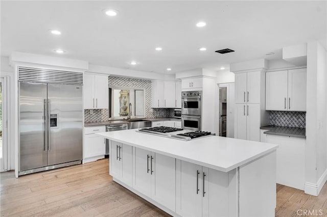 kitchen with decorative backsplash, a center island, light wood-type flooring, and appliances with stainless steel finishes